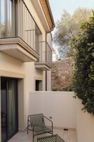 Un edificio moderno con un balcón, una pared de piedra y un seto verde.