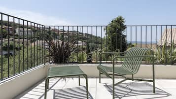 A balcony with two green metal chairs and a small table, overlooking a residential area with houses and greenery.