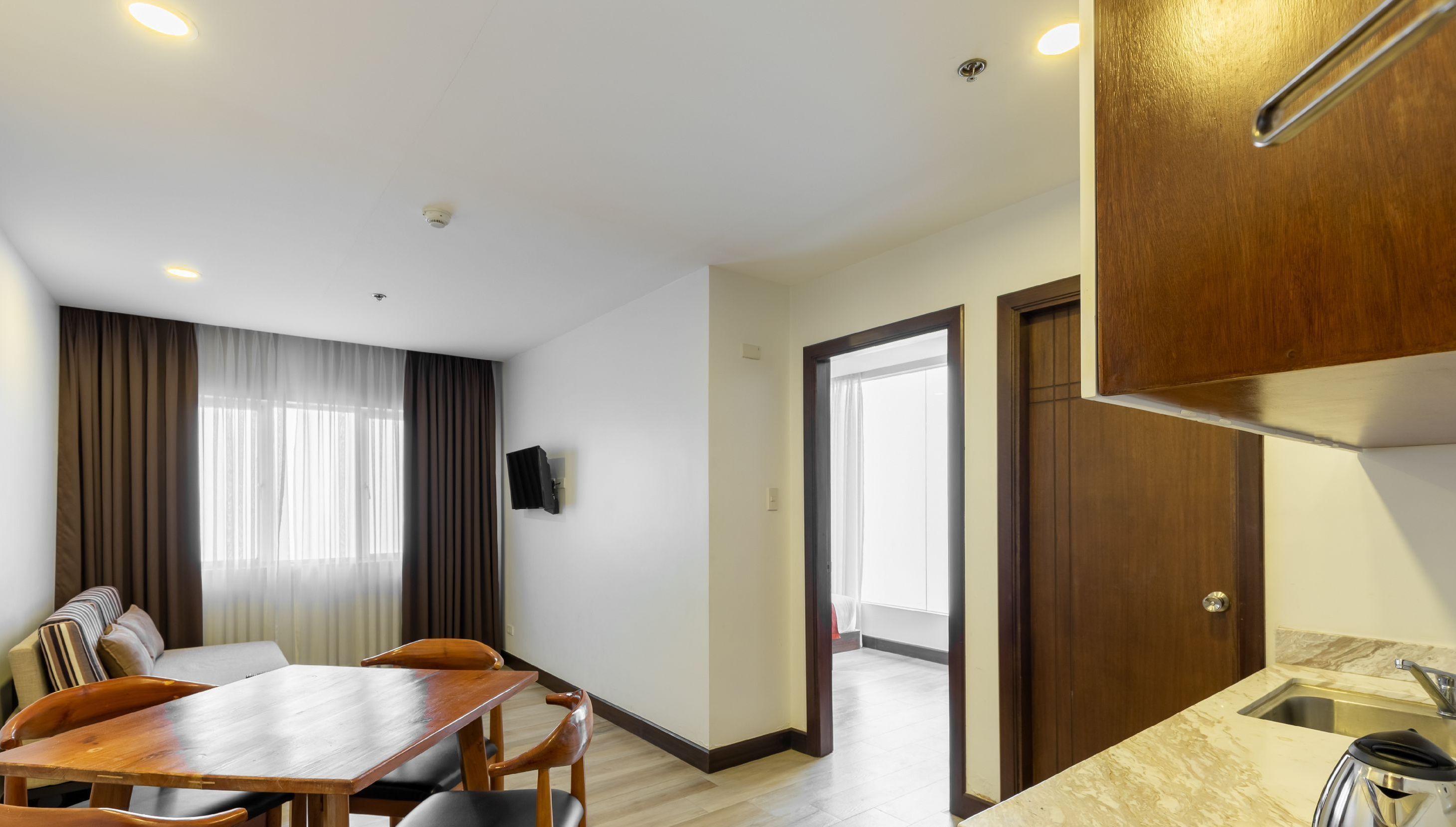 Ein modernes Hotelzimmer mit Essbereich, einem Wandfernseher und einer Küche mit Spüle und Arbeitsplatte.