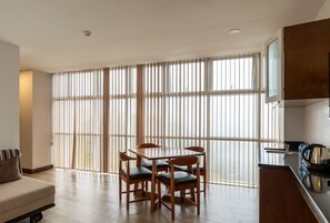 Una cocina moderna con zona de comedor, ventanas amplias con persianas y una mesa de madera con sillas.