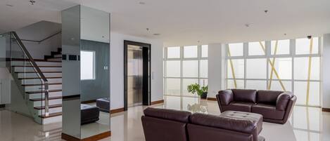Un amplio salón con una escalera moderna, un ventanal con vistas y un sofá de cuero.