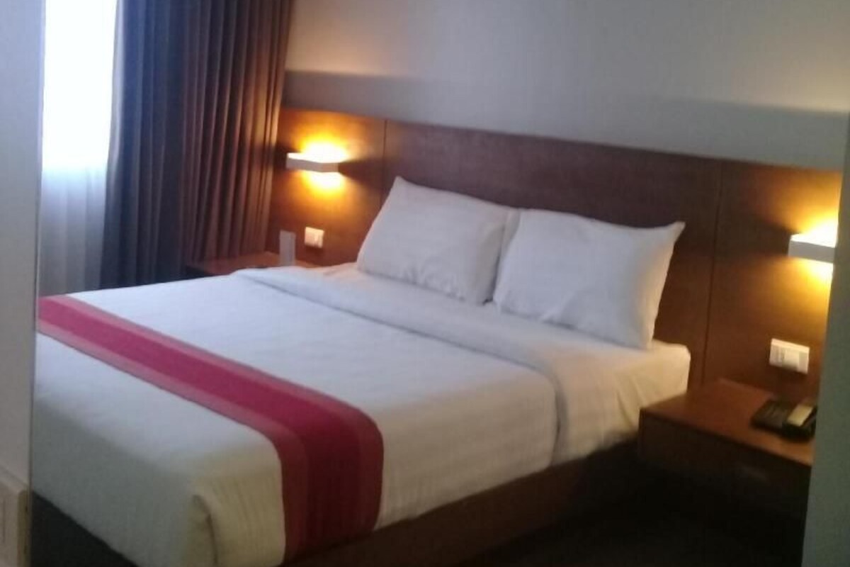 A hotel room with a large bed, bedside lamps, and a nightstand.