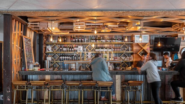Eine Bar mit Holzhocker, Flaschenregalen und einer Kreidetafel mit der Speisekarte.