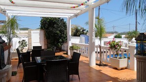 A covered outdoor patio with a table and chairs, surrounded by potted plants and a view of the cityscape. - Hotel Casa Día y Noche (Calpe)