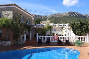 A swimming pool with a white fence and chairs, surrounded by buildings with stone walls and a mountainous backdrop. - Hotel Casa Día y Noche (Calpe)