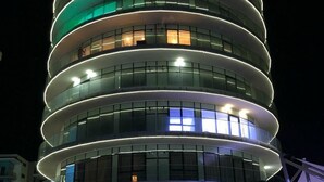 A modern hotel with a circular design, multiple balconies, and a well-lit entrance area with outdoor seating. - White Tower Mamaia (Navodari)