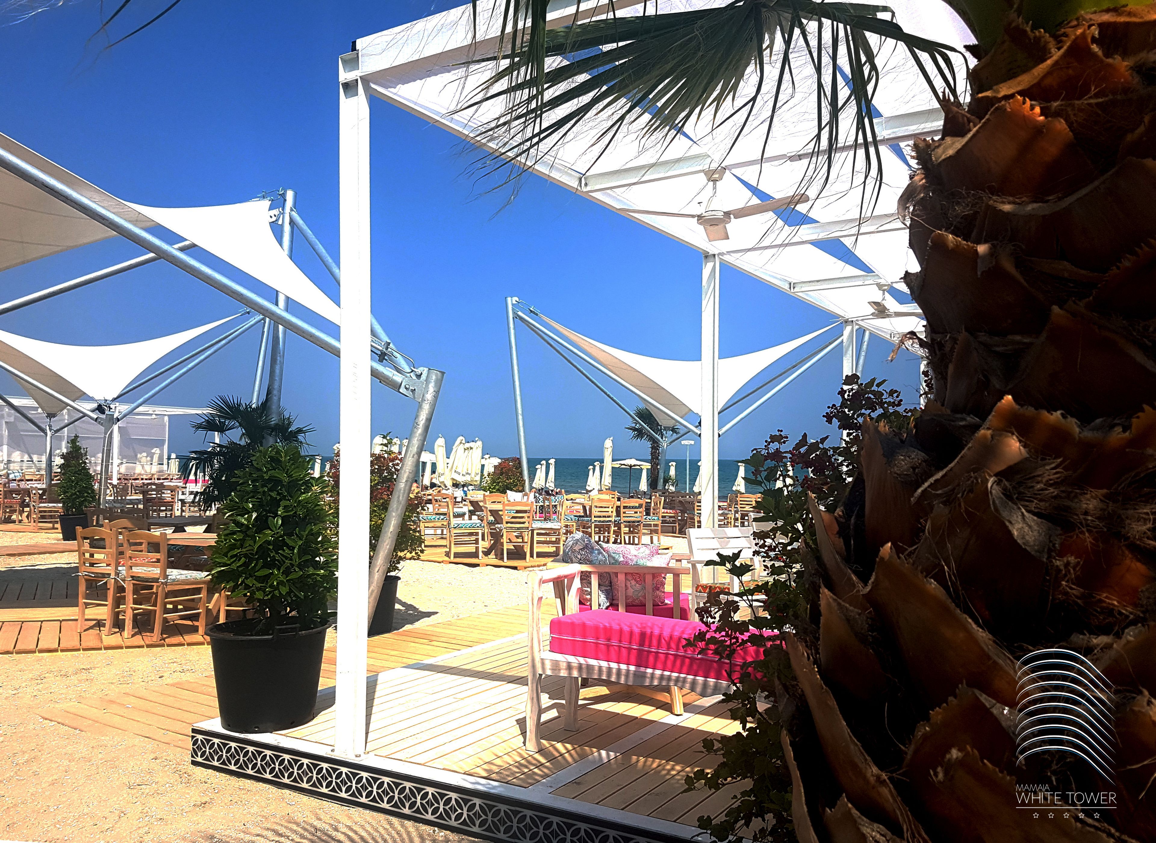 An outdoor seating area with tables and chairs, umbrellas, and potted plants.
