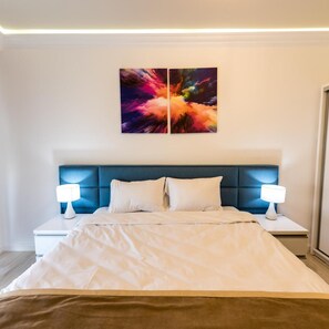 A modern bedroom with a large bed, two bedside lamps, and a vibrant abstract painting above the headboard. - White Tower Mamaia (Navodari)