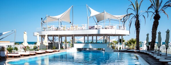A rooftop pool area with lounge chairs and umbrellas, overlooking the sea.