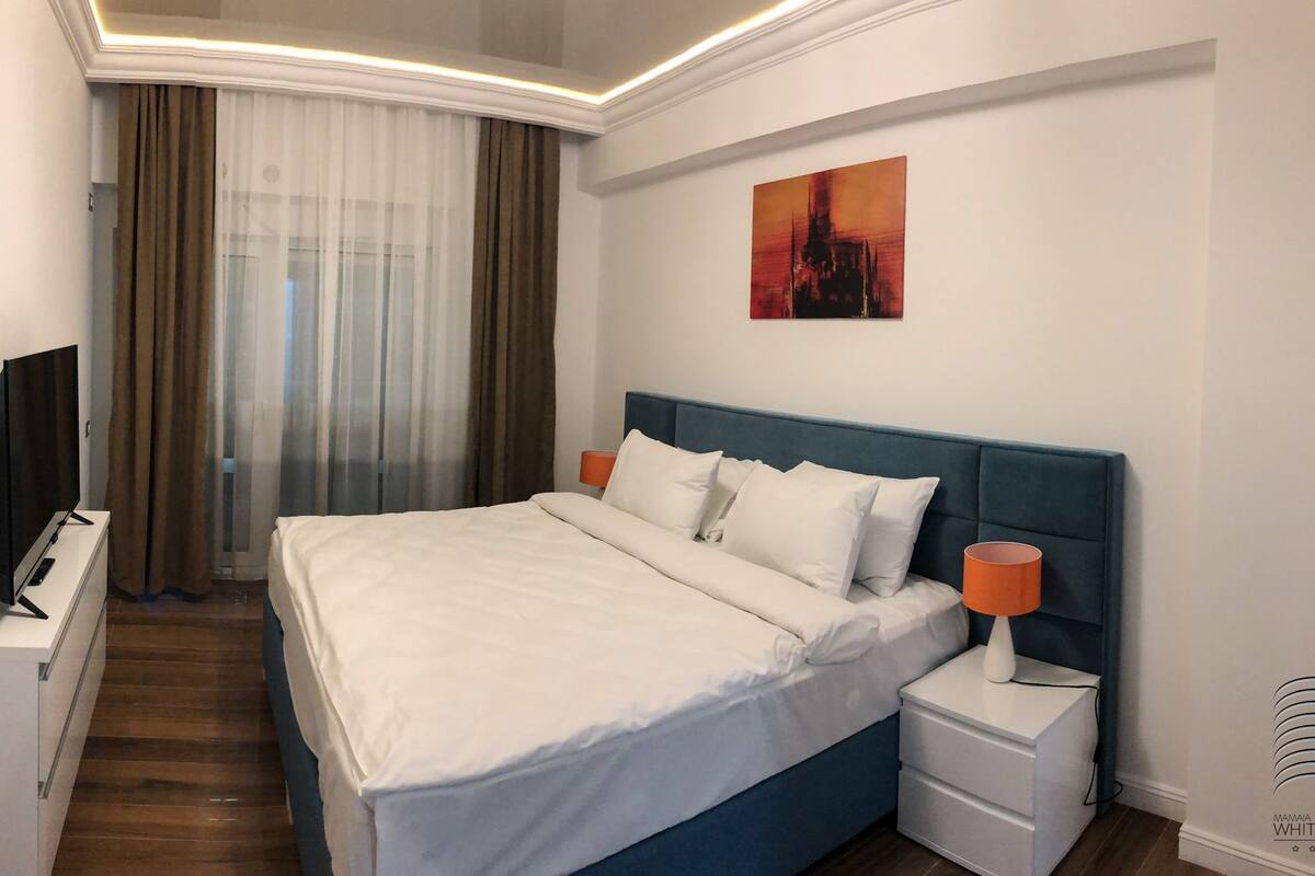 A hotel room with a bed, a TV, a nightstand, and a painting on the wall.