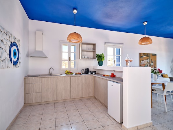 A modern kitchen with a blue ceiling, wooden cabinets, a white countertop, and two hanging pendant lights. - Aria Kimolos Residence (Kimolos)