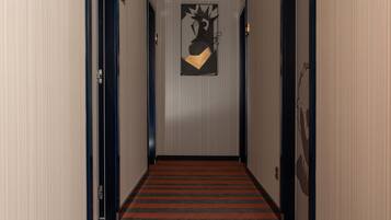 Un pasillo con alfombra roja, puertas a ambos lados y una obra de arte colgada en la pared.