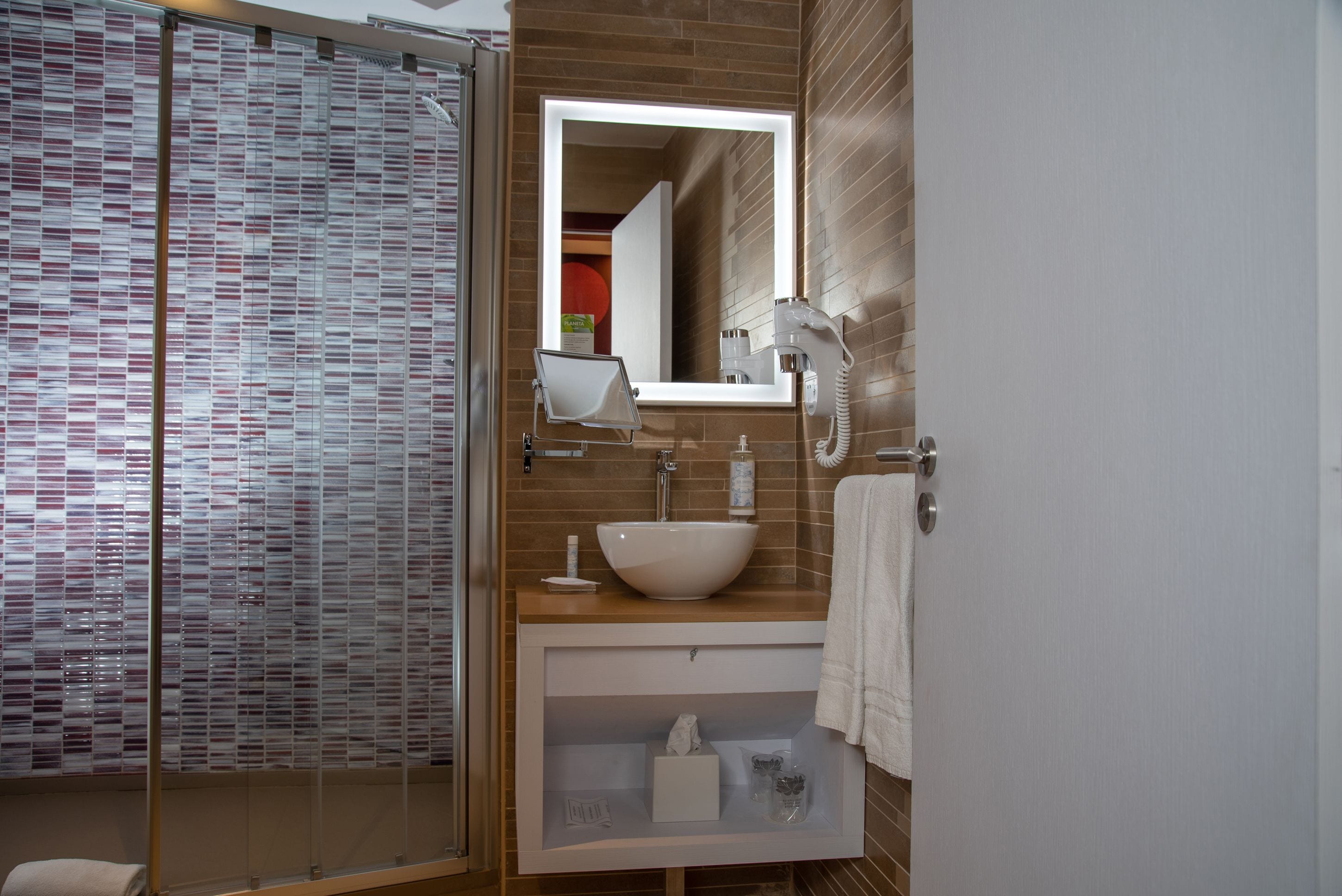 Un baño moderno con cabina de ducha de vidrio, un lavabo blanco e iluminación integrada en el espejo.