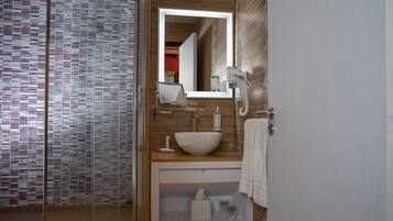 Un baño moderno con cabina de ducha de vidrio, un lavabo blanco e iluminación integrada en el espejo.