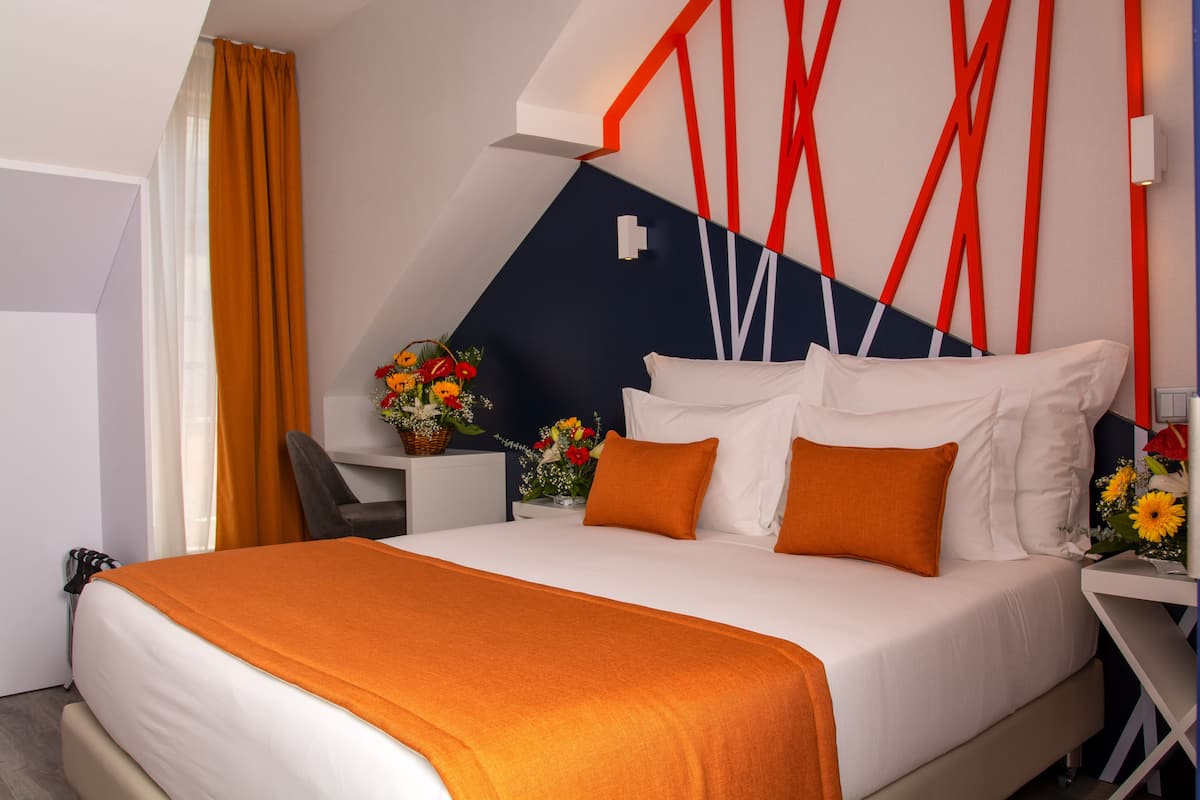 A modern hotel room with a large bed, orange bedding, a desk with a chair, and a decorative wall.