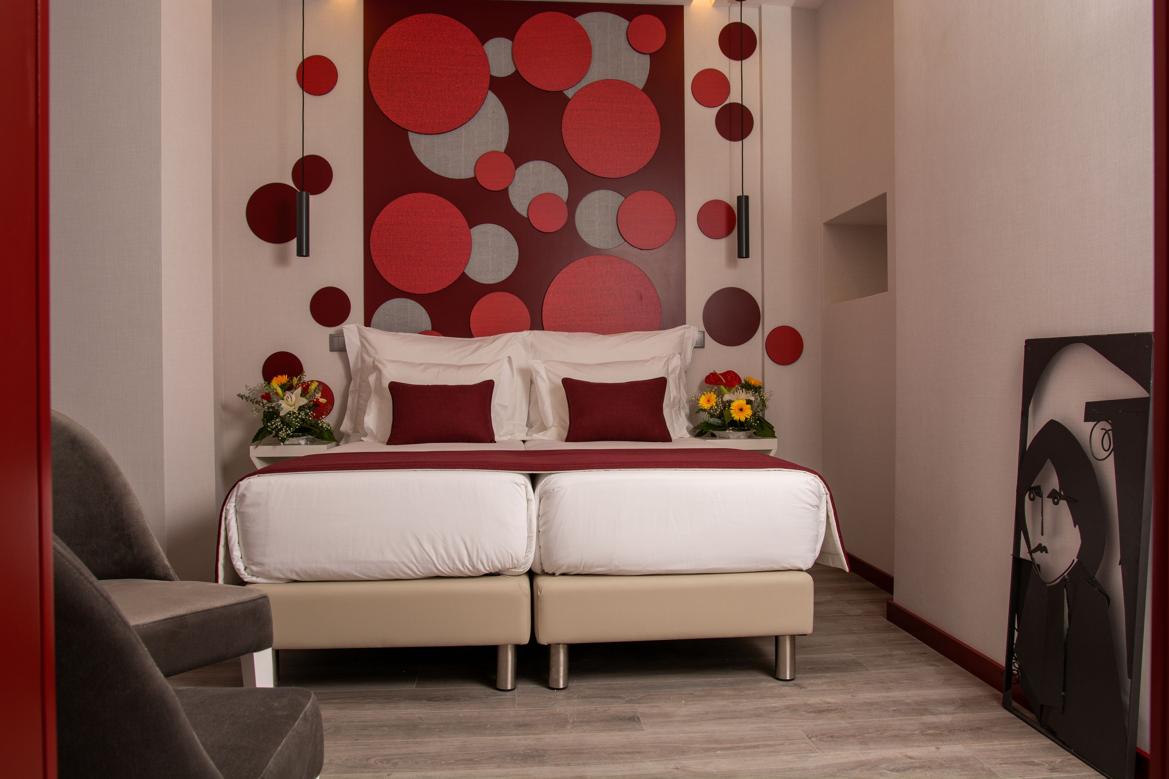 A modern bedroom with a double bed, two bedside tables, a red and white wall decoration, and a small side table with flowers.