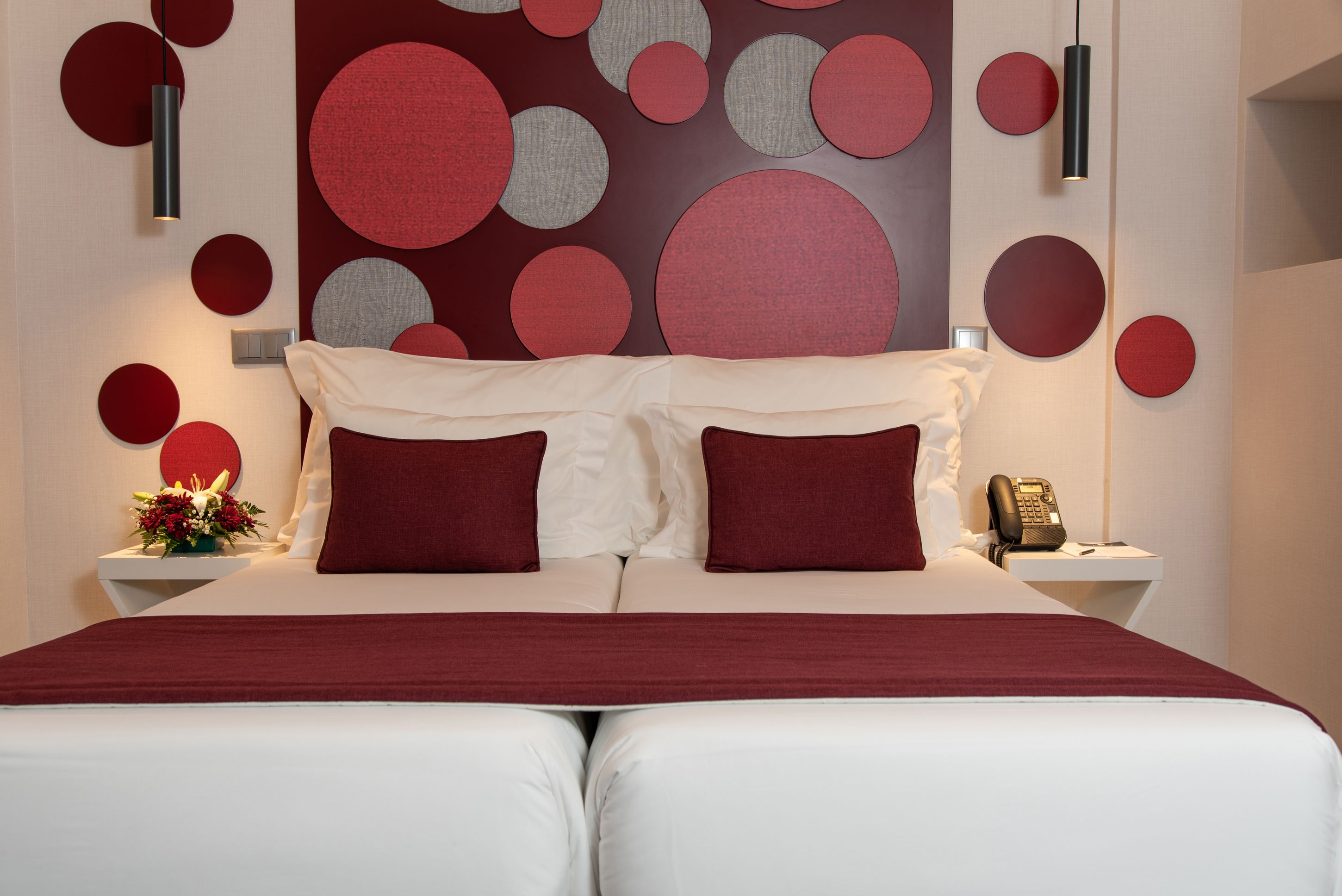 Une chambre d’hôtel avec un grand lit, deux oreillers, une table de chevet avec un téléphone et un mur orné de motifs circulaires.