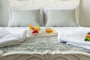 A neatly made bed with white linens, a tray with fruit and a glass of juice, and a bottle of orange juice on the side. - Grande Casa 1926 (Chania)