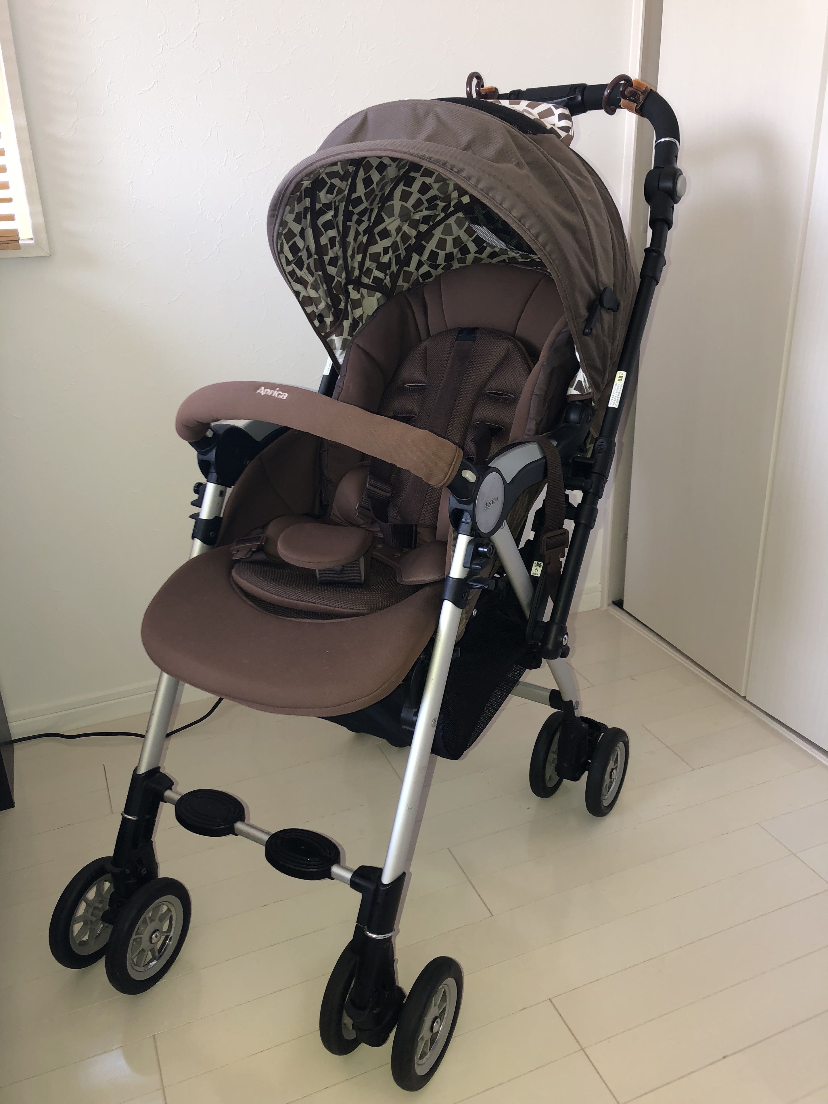 A stroller with a patterned canopy and a brown seat, equipped with a canopy cover and a padded seat.