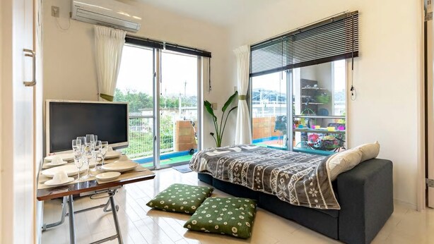 Une chambre moderne avec un lit, un bureau équipé d’un ordinateur et une grande fenêtre donnant sur l’extérieur.