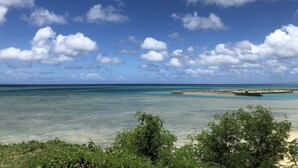 Une plage aux eaux turquoise et limpides, une île lointaine et quelques nuages épars.