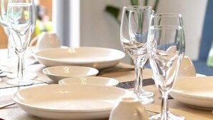 Une table à manger dressée avec des assiettes, des bols et des verres à vin, et une plante en arrière-plan.