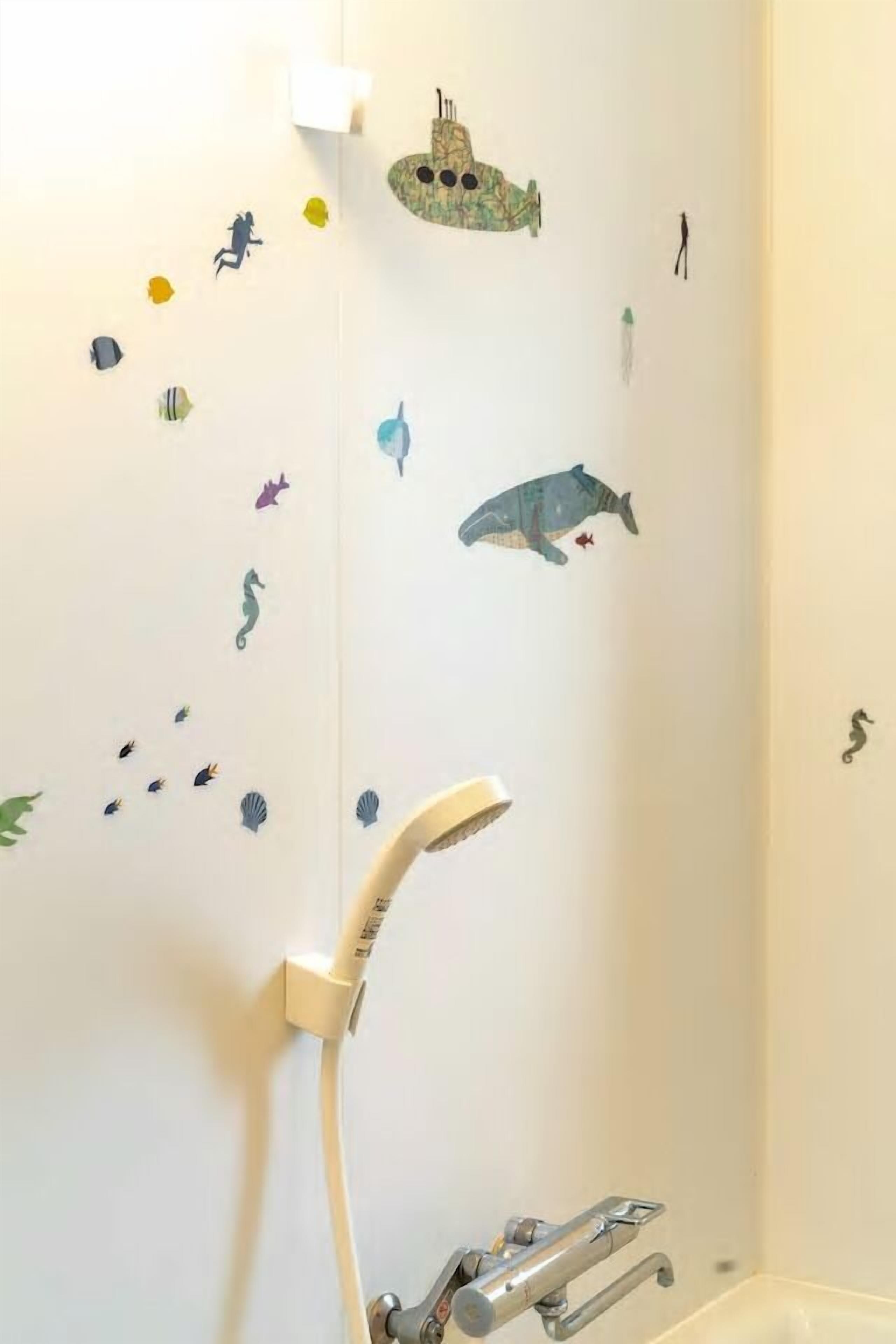 A bathroom with a shower, a bathtub, and a wall decorated with marine life stickers.