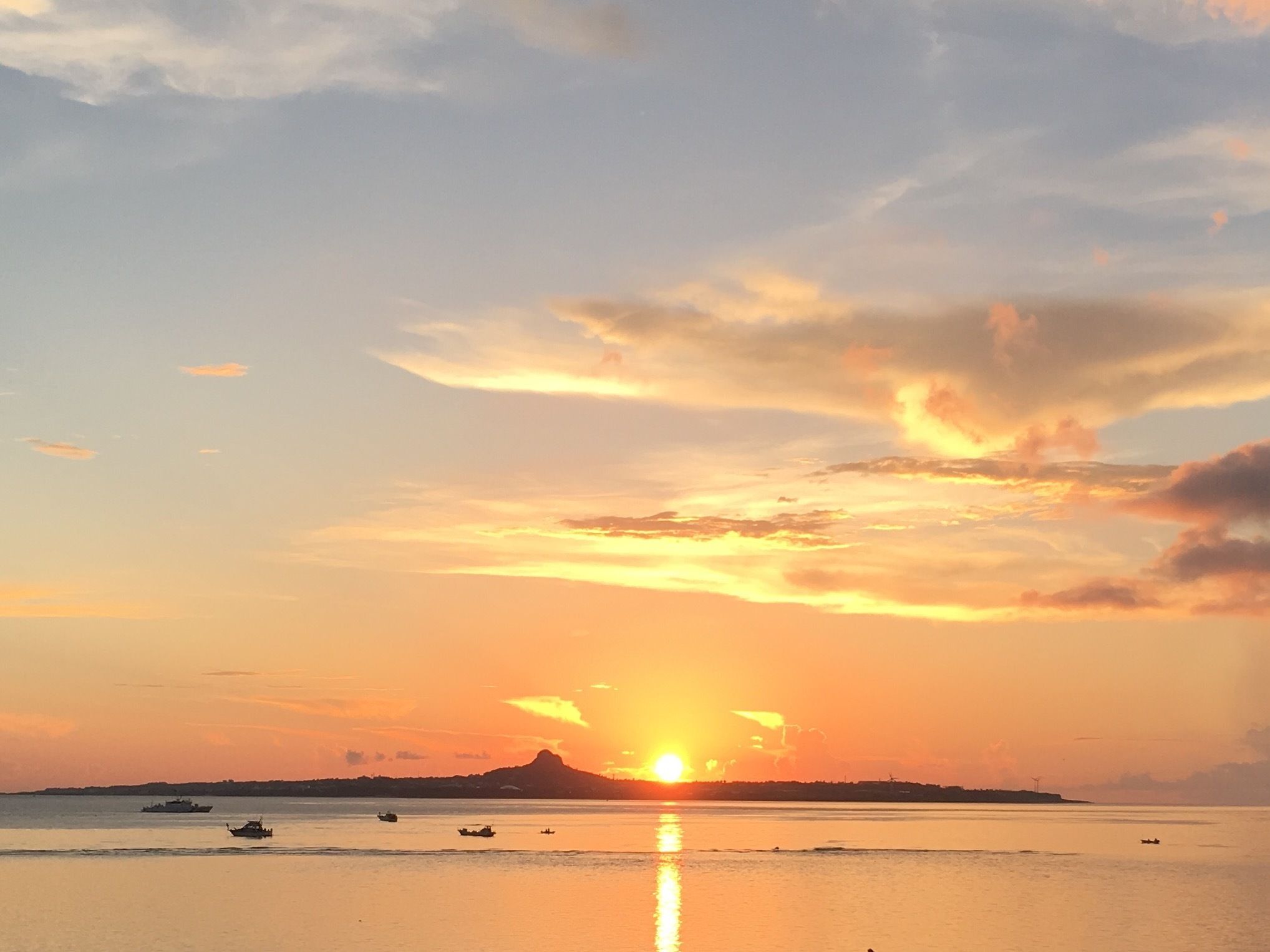 A sunset over a calm sea with boats and a distant landmass.