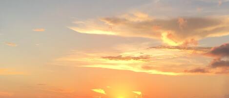 A sunset over a calm sea with boats and a distant landmass.