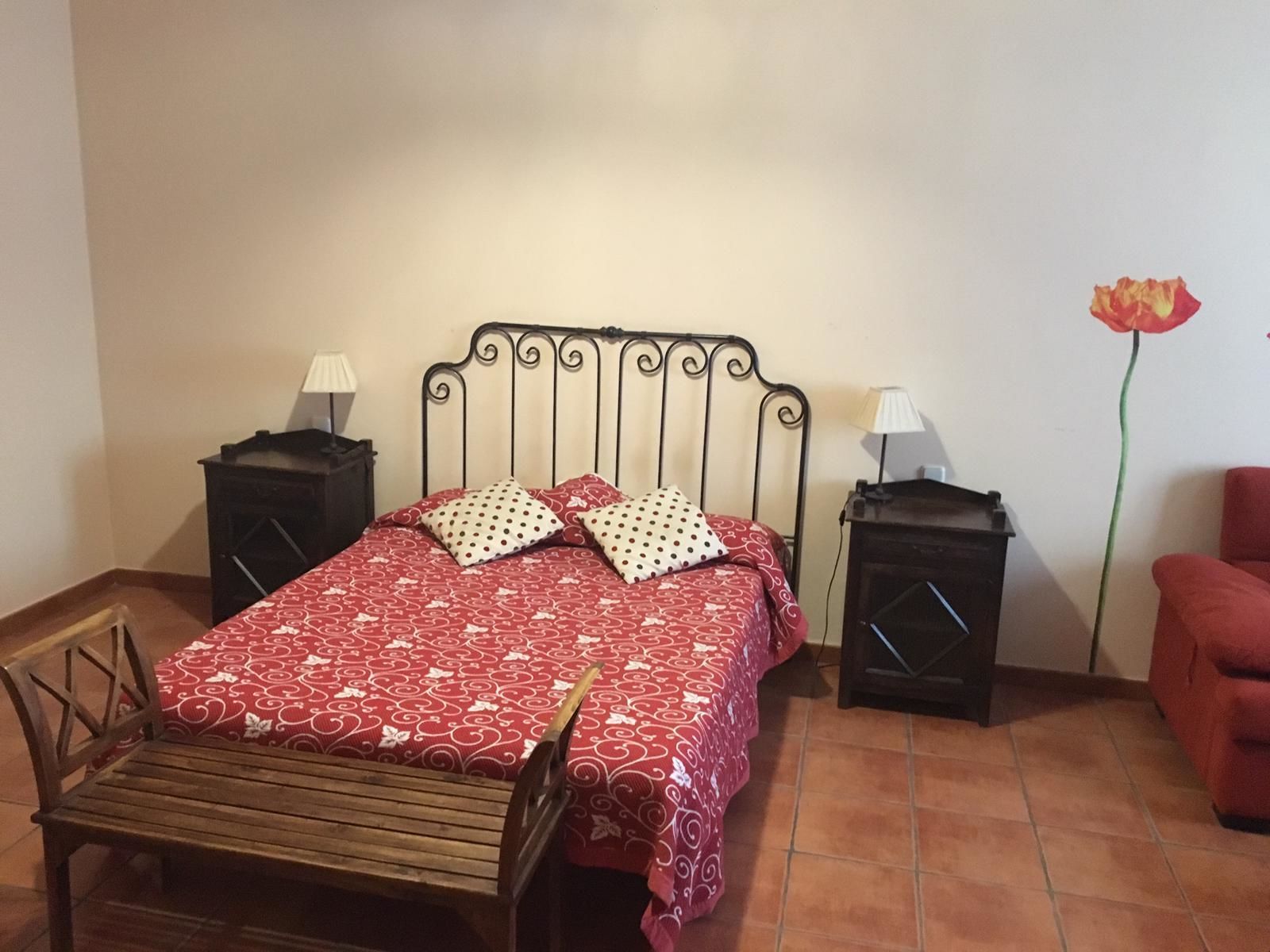 A bedroom with a bed, two nightstands, a wooden chair, and a red armchair.