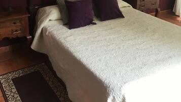 Un dormitorio con una cama, dos mesitas de noche, una lámpara roja, una mesita de noche de madera y una alfombra estampada.