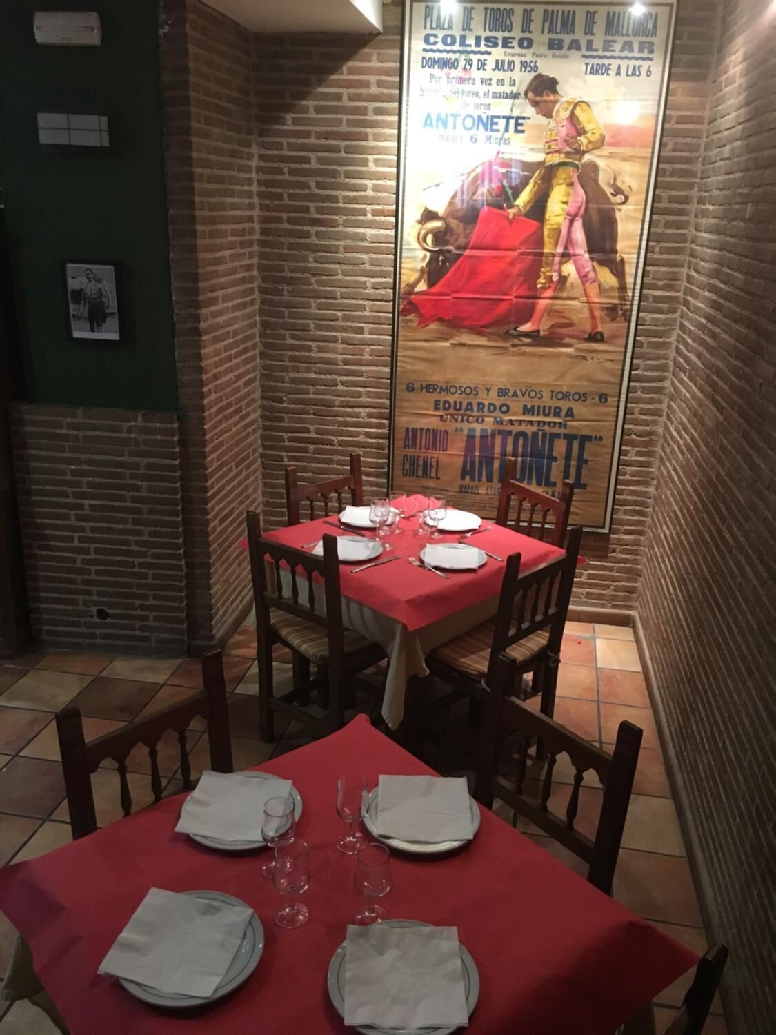 Ein Restaurantinneres mit einem für vier Personen gedeckten rotem Tisch, Ziegelwänden und einem Plakat, das eine Stierkampfveranstaltung bewirbt.
