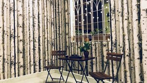 Una habitación con papel tapiz estampado con motivos de abedul, una ventana con diseño de cuadrícula blanca y dos sillas de madera junto a una mesita.
