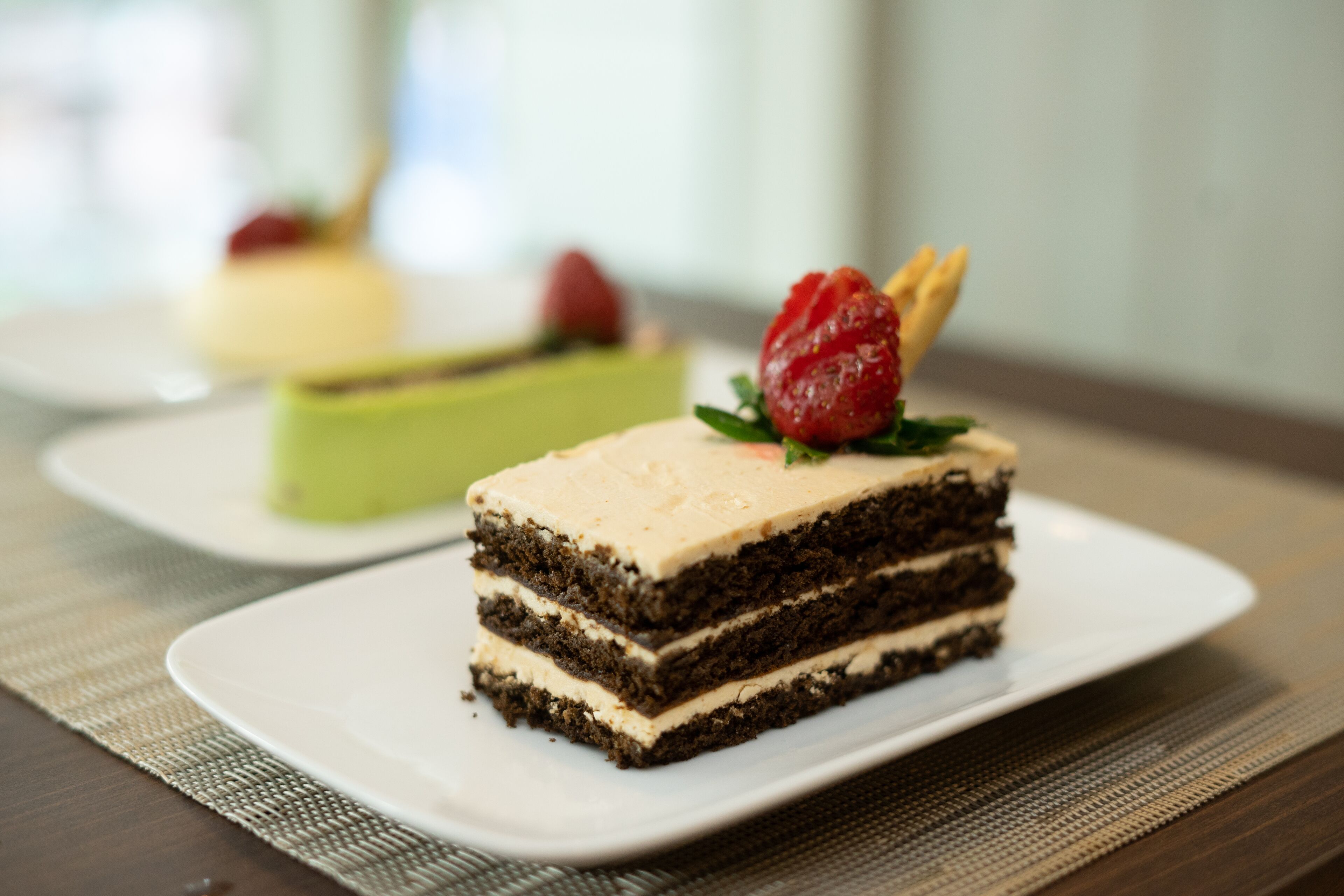 Une part de gâteau à plusieurs couches, surmontée d’une fraise, posée sur une assiette blanche.