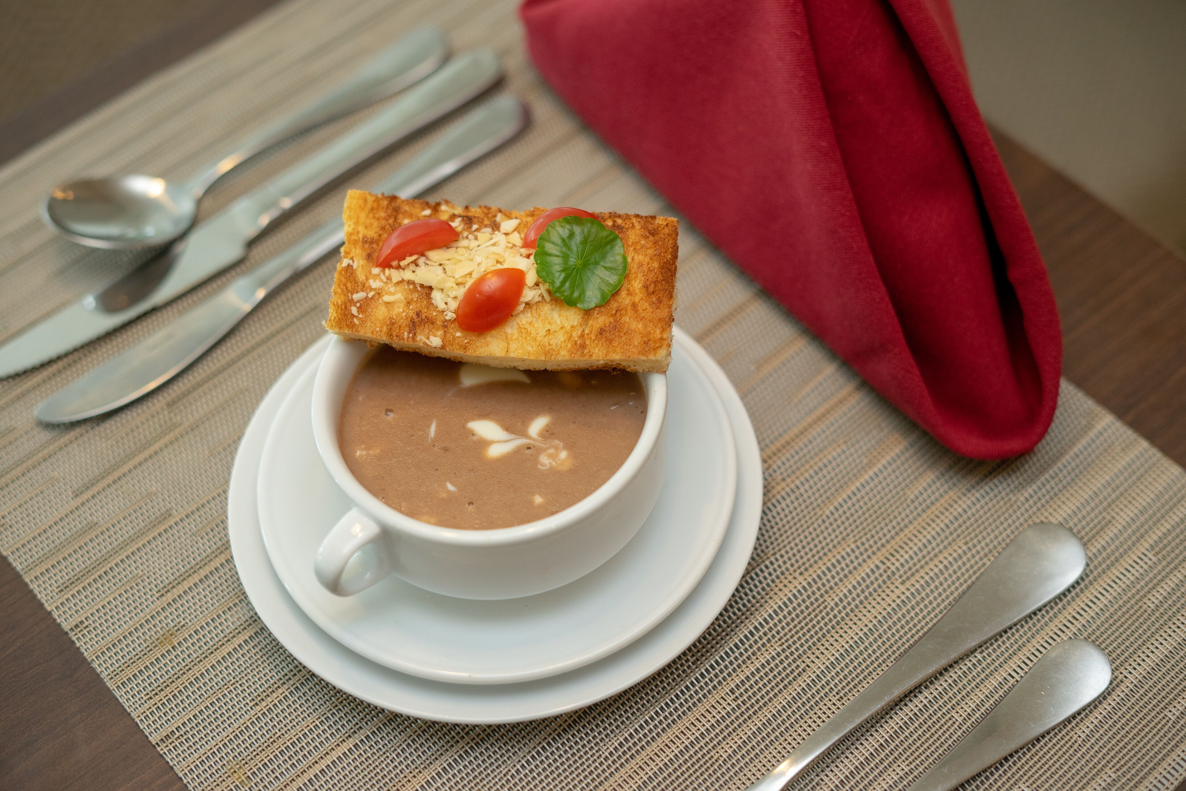Una tazza di caffè con una fetta di pane tostato condita con pomodori e una foglia, su un piattino bianco.