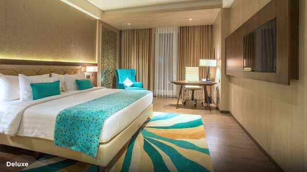 A hotel room with a large bed, a desk, a chair, a TV, and a patterned rug. - BW Luxury Jambi (Jambi)