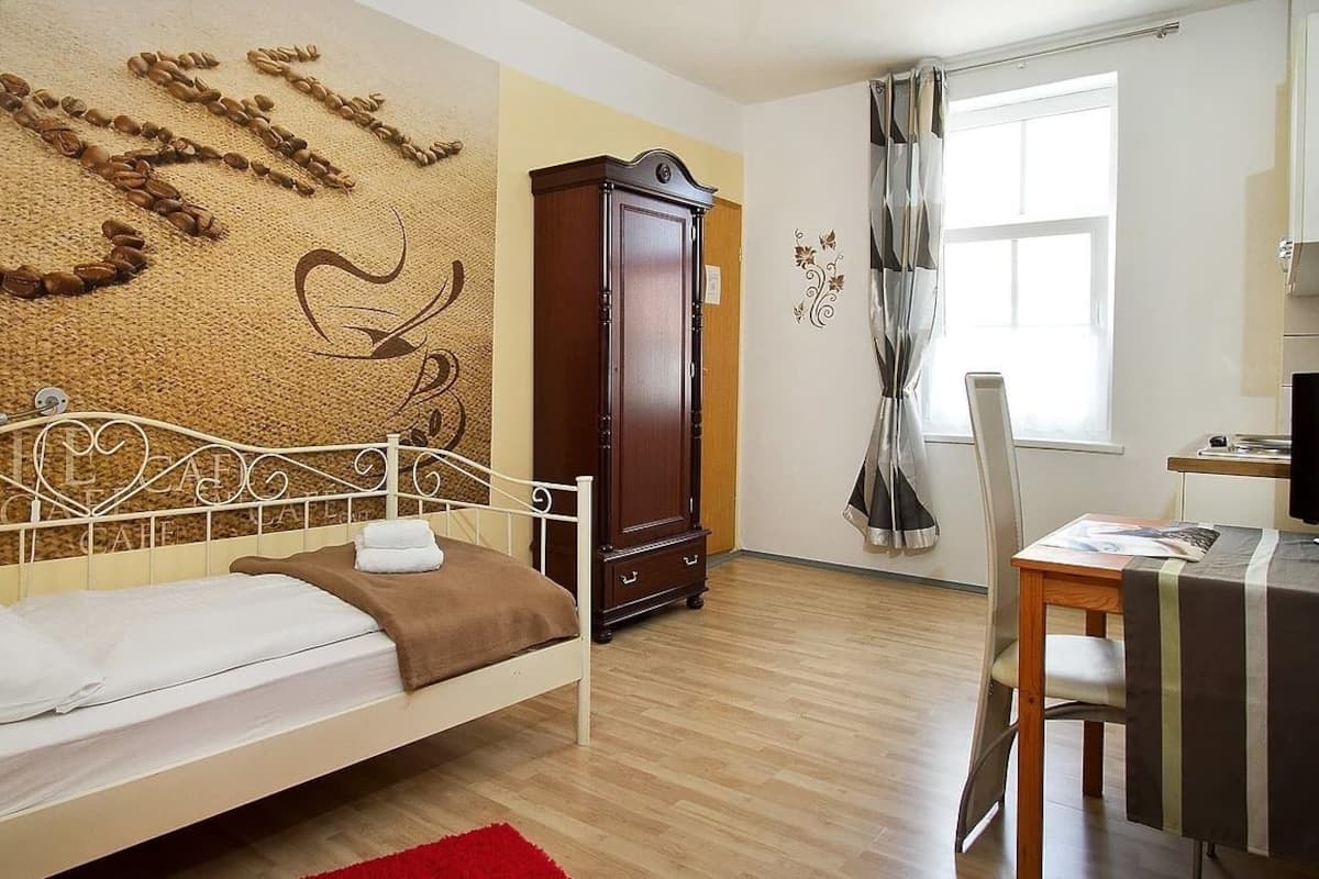 A bedroom with a bed, a wardrobe, a desk with a chair, a TV, and a window with curtains.