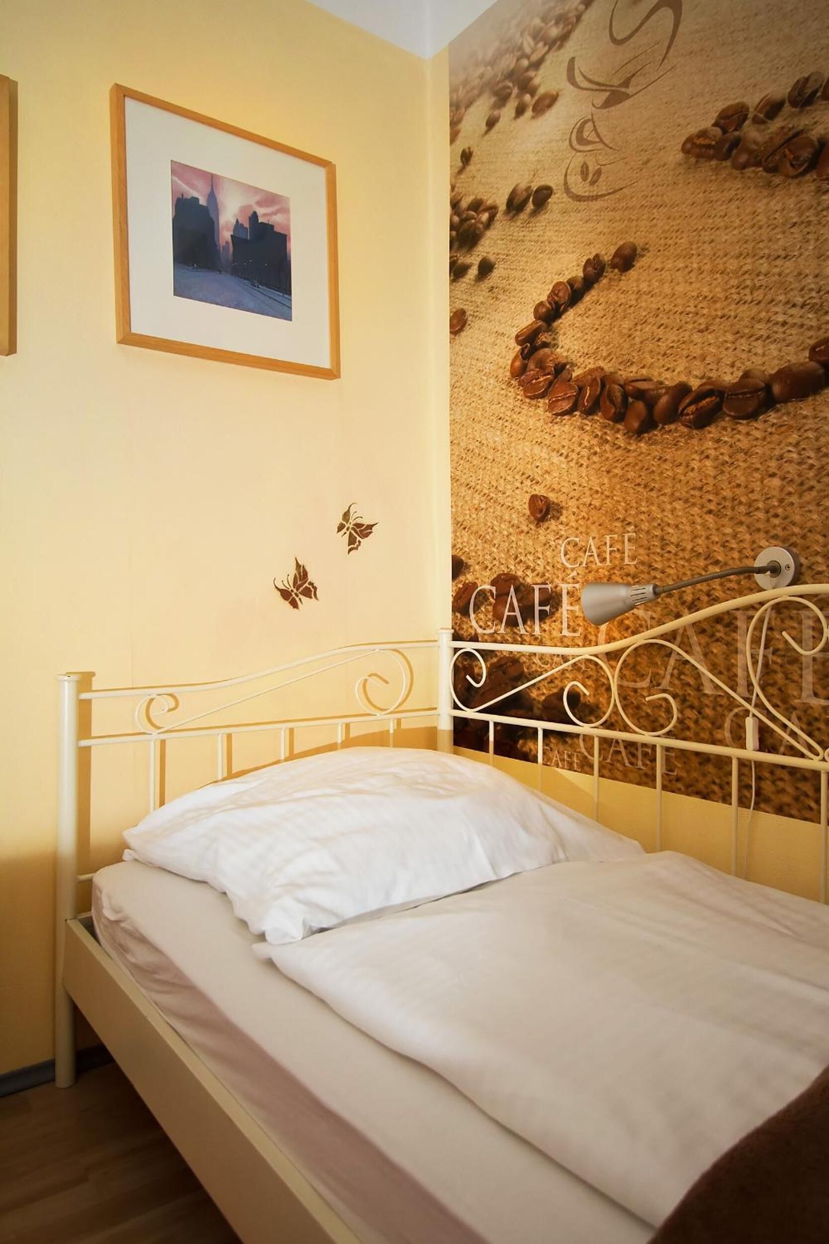 Una cama con cabecera blanca, un cuadro en la pared y un adorno de pared con granos de café y la palabra "CAFE".
