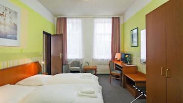 Habitación de hotel con dos camas, un escritorio con una computadora, una silla y un ventanal con cortinas.