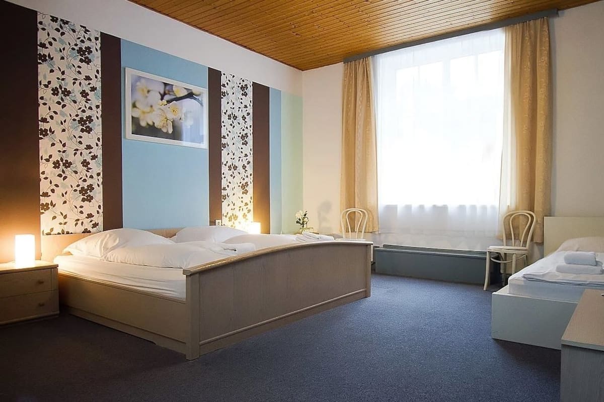 A hotel room with a large bed, bedside tables, a desk, a chair, and a window with curtains.