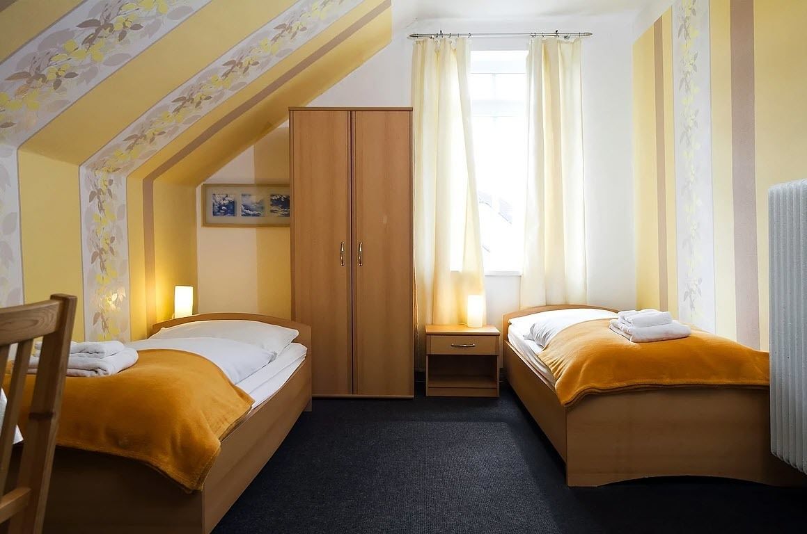 Habitación de hotel con dos camas, un armario, una mesita y una ventana con cortinas.