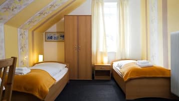 Habitación de hotel con dos camas, un armario, una mesita y una ventana con cortinas.