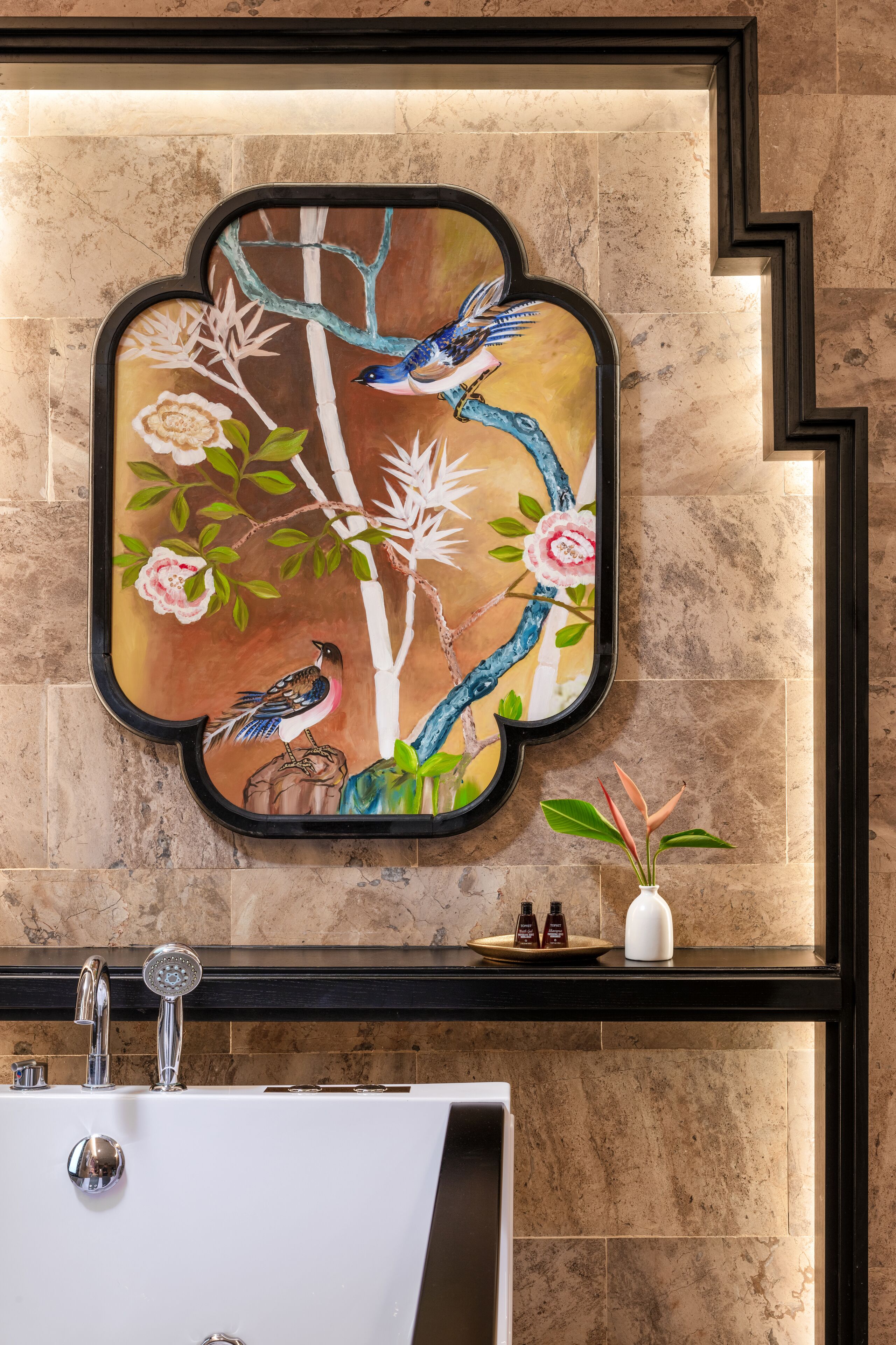 A bathroom with a modern sink, a decorative wall piece, and a vase with flowers.