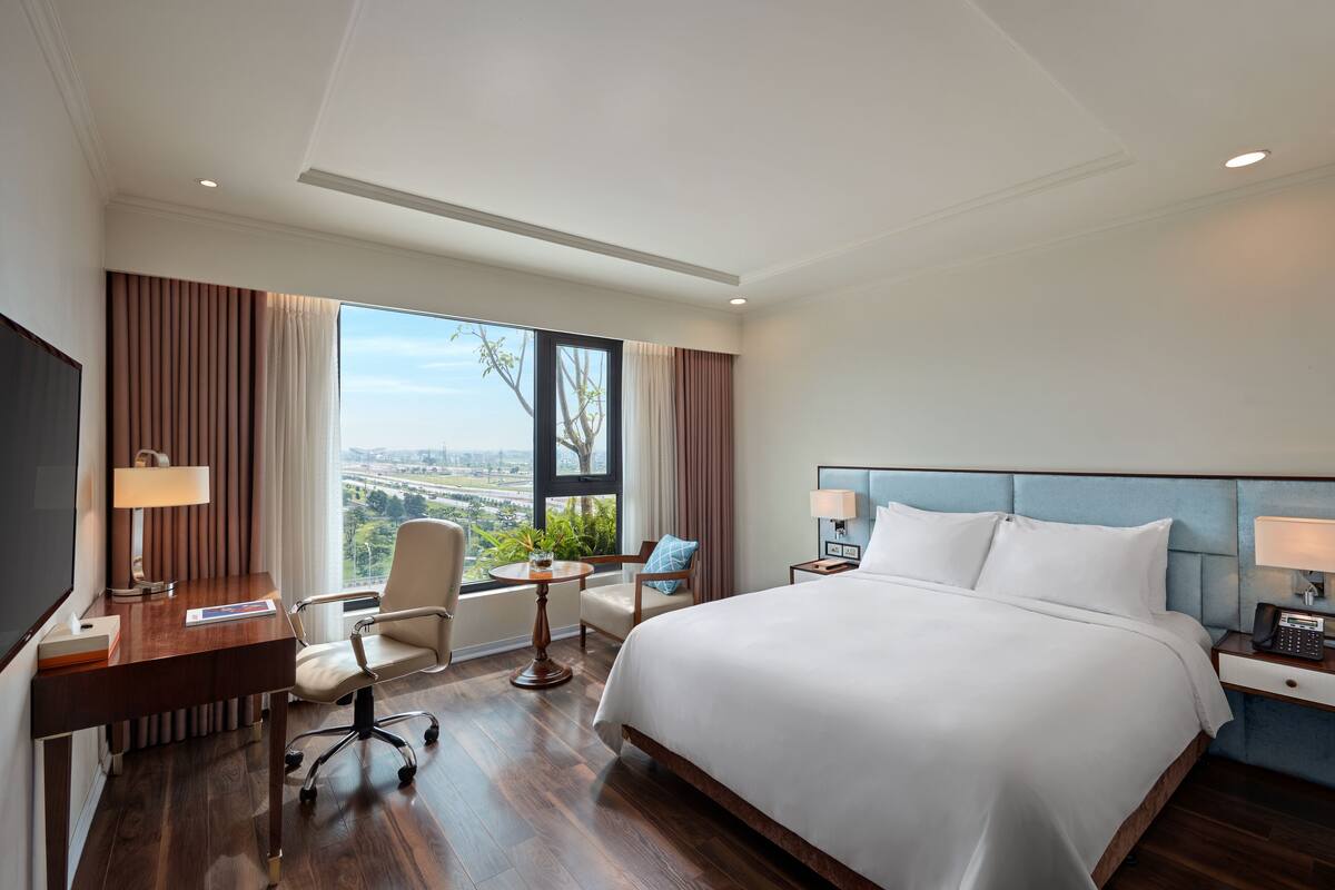 Quarto de hotel com uma cama grande, uma escrivaninha, uma cadeira, uma mesinha e vista para a cidade.
