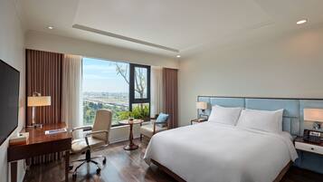 A hotel room with a large bed, a desk, a chair, a small table, and a view of the city.