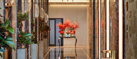 A polished marble hallway with a reflective floor, a central seating area with red flowers, and modern wall sconces.