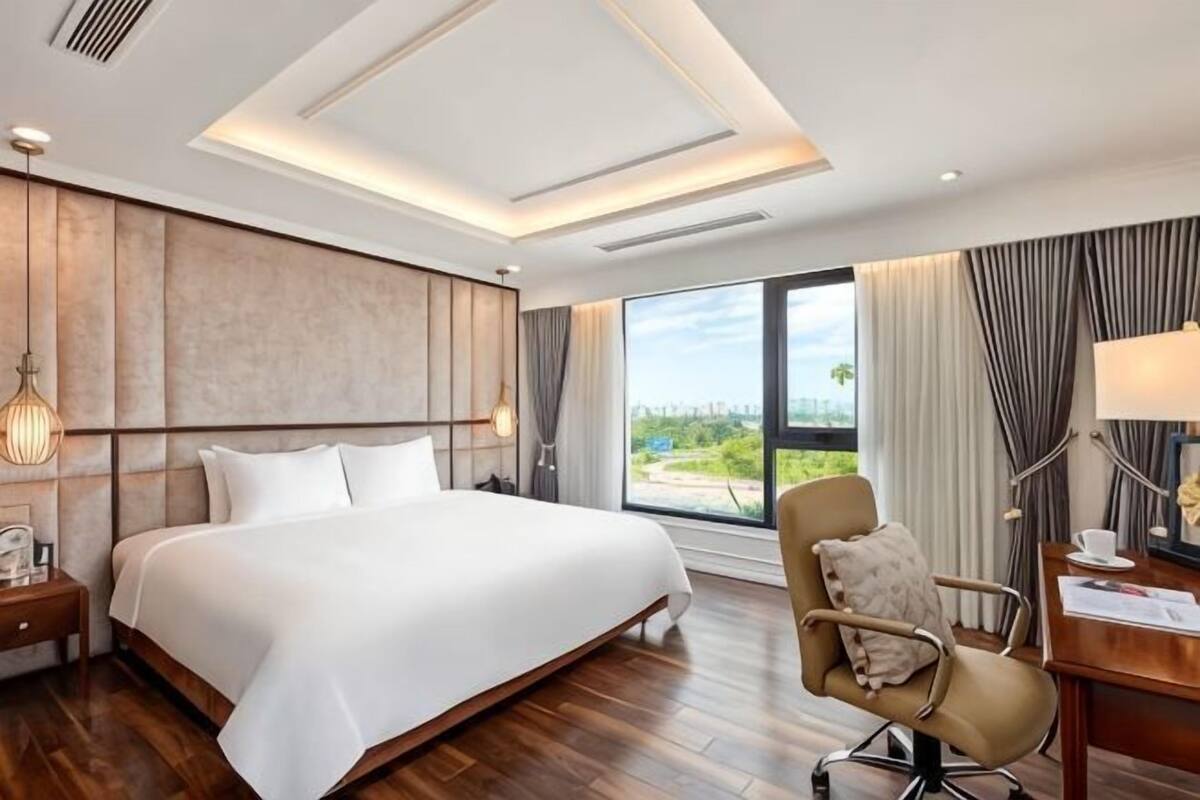 A hotel room with a large bed, a desk, a chair, and a view of the outdoors.