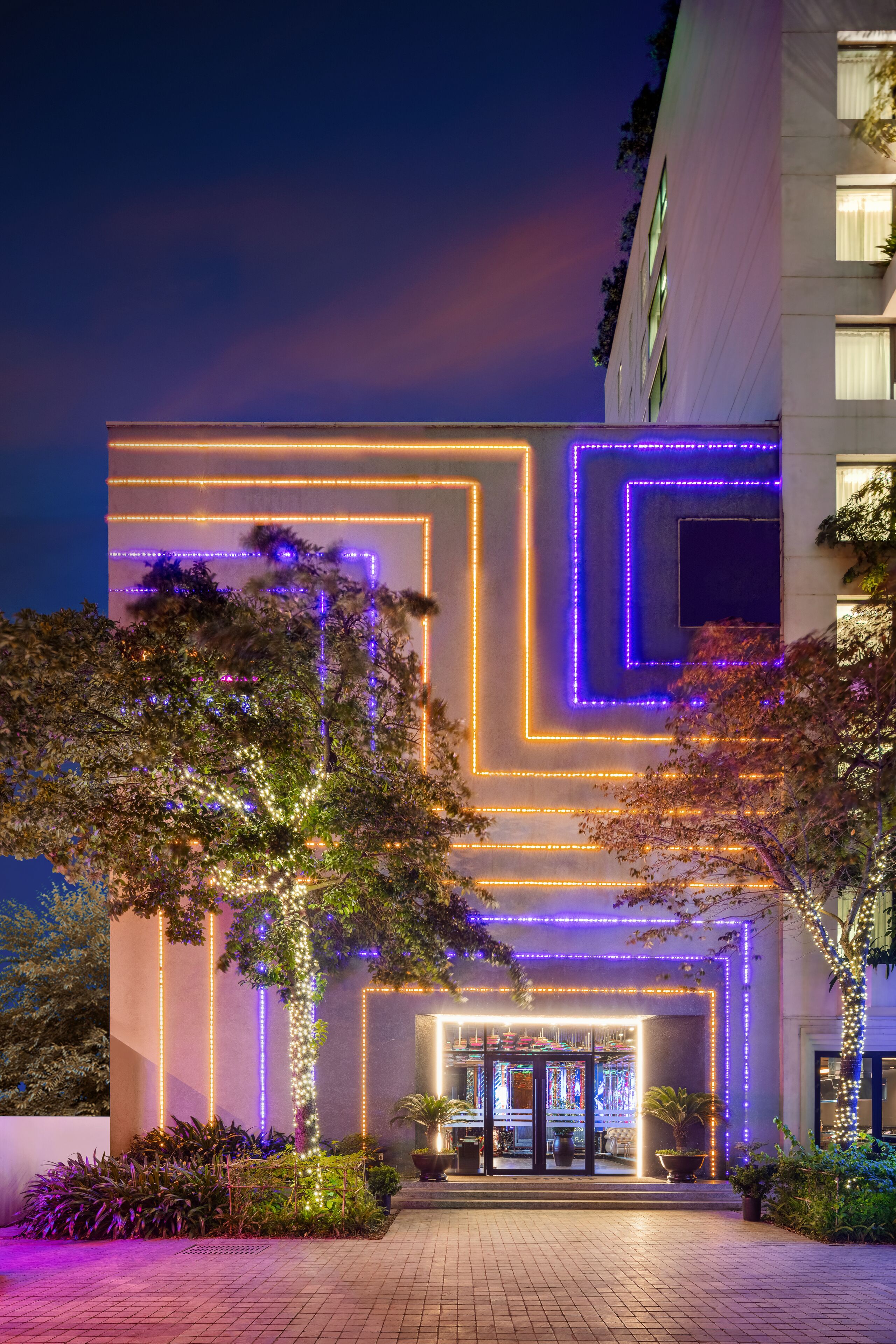 A modern building with illuminated geometric patterns on the facade, a well-maintained entrance area with potted plants, and a clear view of the building's entrance.