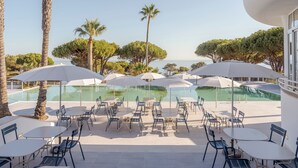 An outdoor pool area with multiple tables and chairs, surrounded by palm trees and umbrellas. - Hapimag Resort Albufeira (Albufeira)