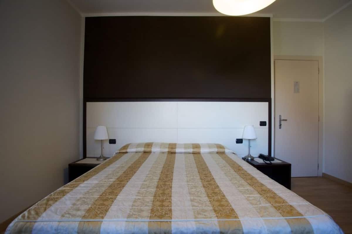 A hotel room with a large bed, two bedside tables, a dark headboard, and a door.